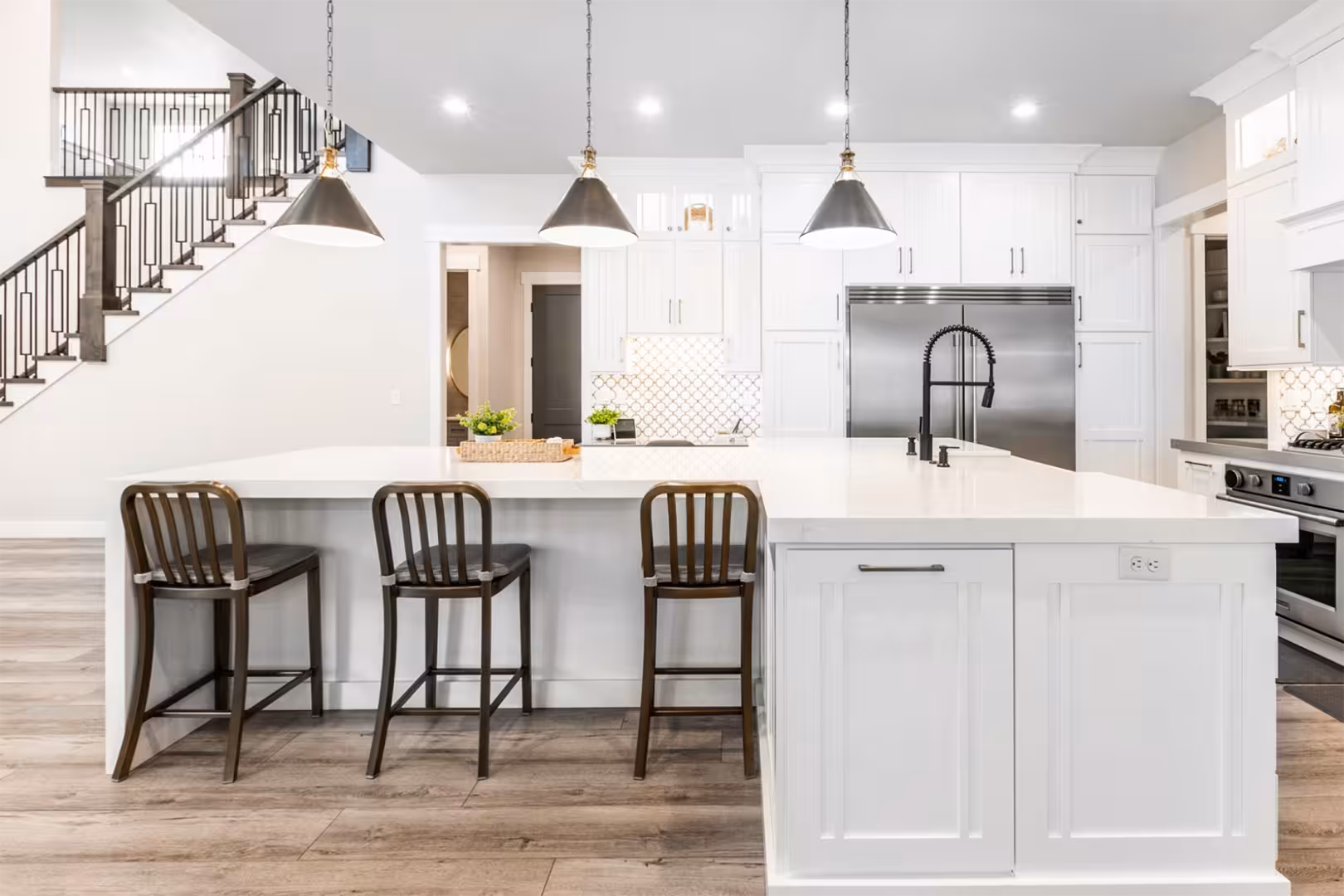 White kitchen in the Alpine home with a large quartz island, black pendants and wood stools