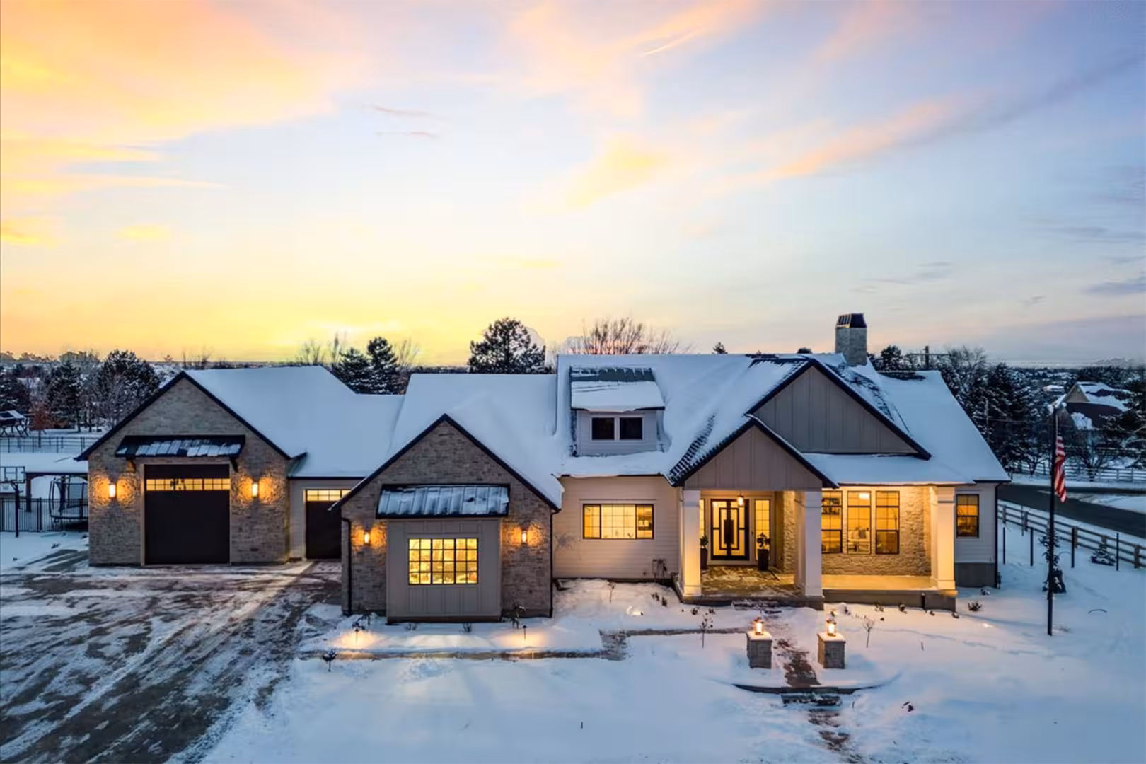 Aerial view of the Bountiful home at dusk in snow, with stone gables and a lit front porch