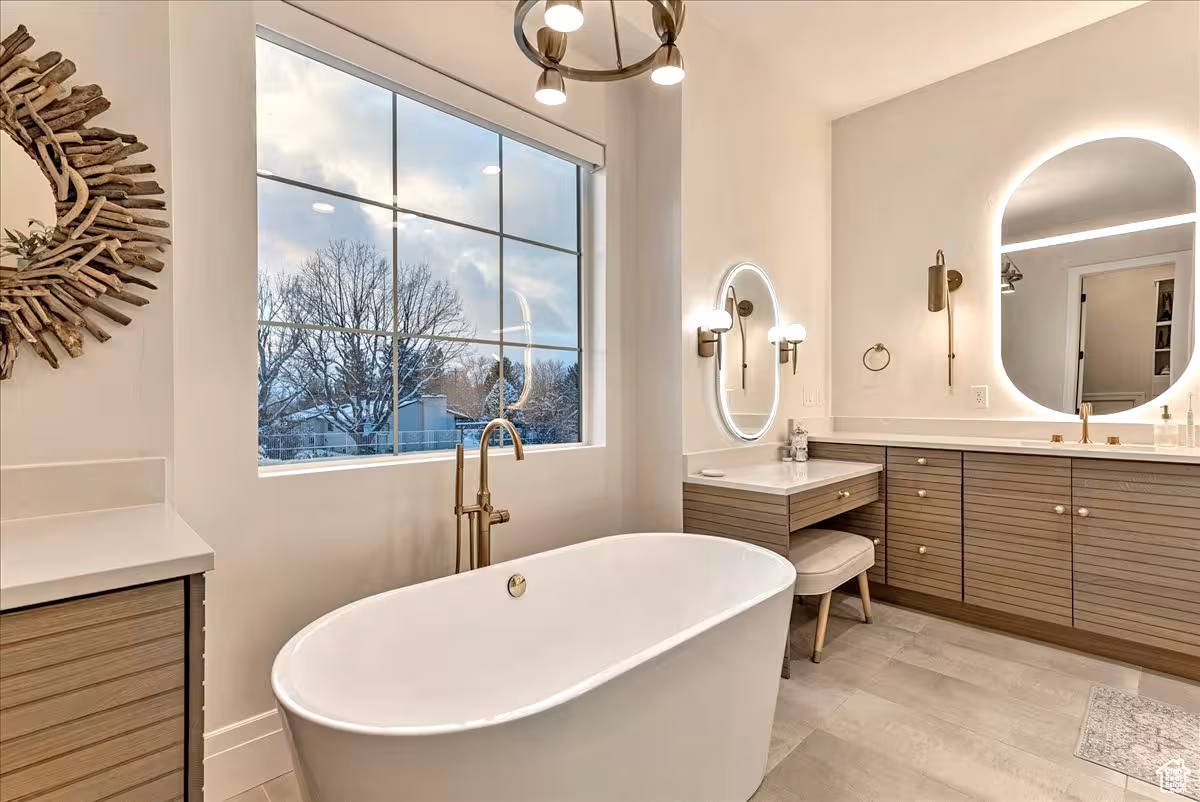 Freestanding tub below a large window in the Bountiful primary bathroom, with a wood vanity