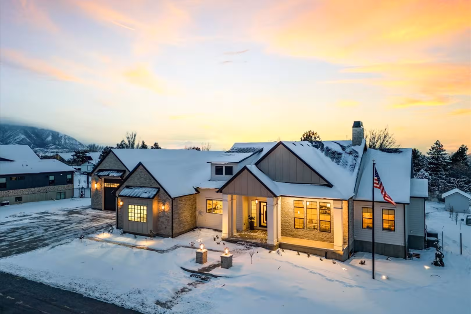 Bountiful home exterior at sunset with snow on the roof, warm window light and a flagpole