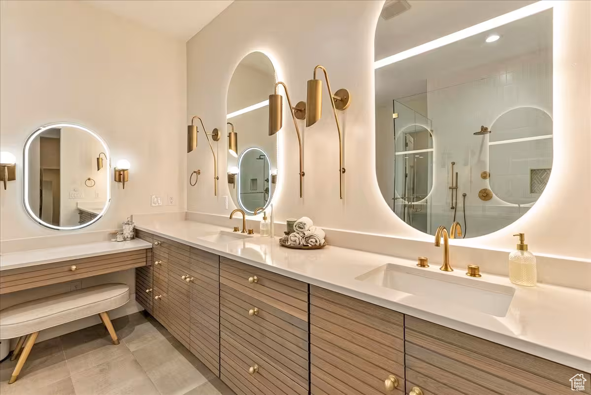 Backlit oval mirrors and brass wall sconces over the fluted wood vanity in the Bountiful home