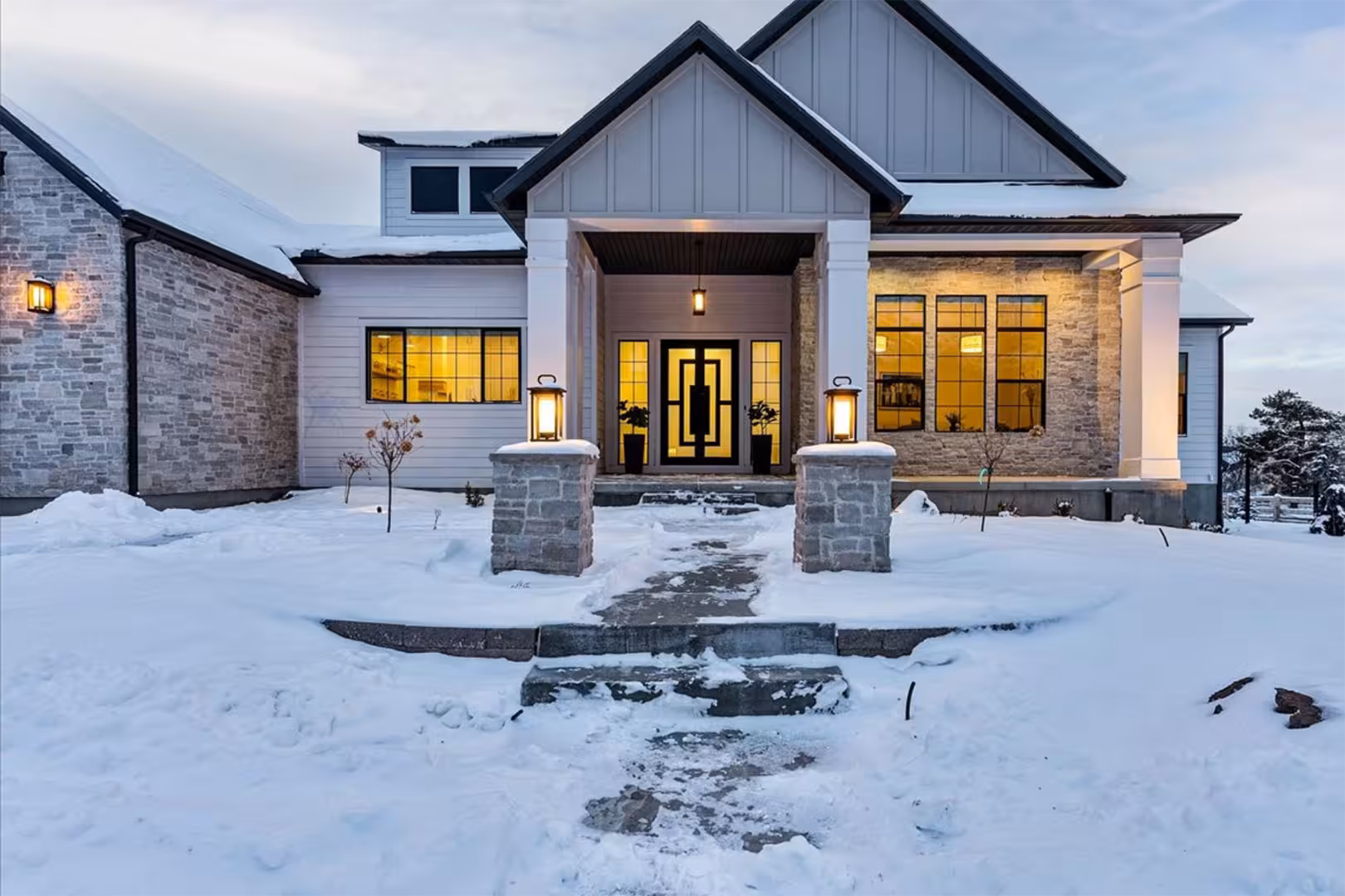 Front entry of the Bountiful home with stone pillars, gray board and batten gable and a black door