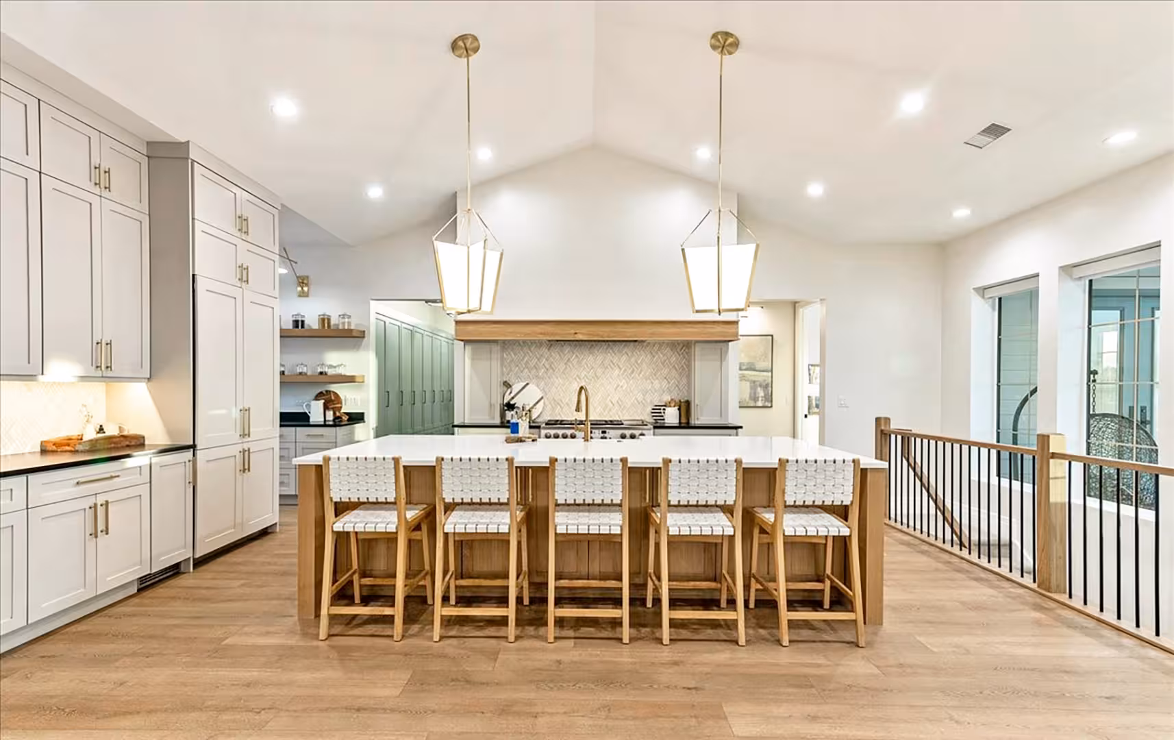 Bountiful home kitchen with a long wood island, woven counter stools and glass lantern pendants