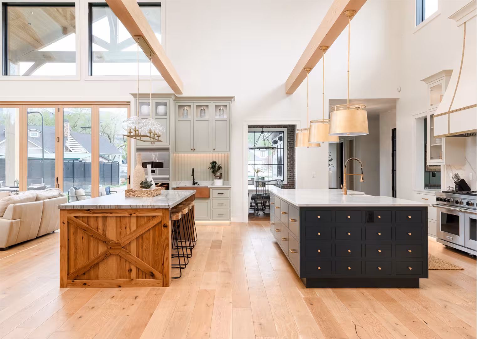 Two-story kitchen in the Draper home with wood beams, brass pendants and a navy island