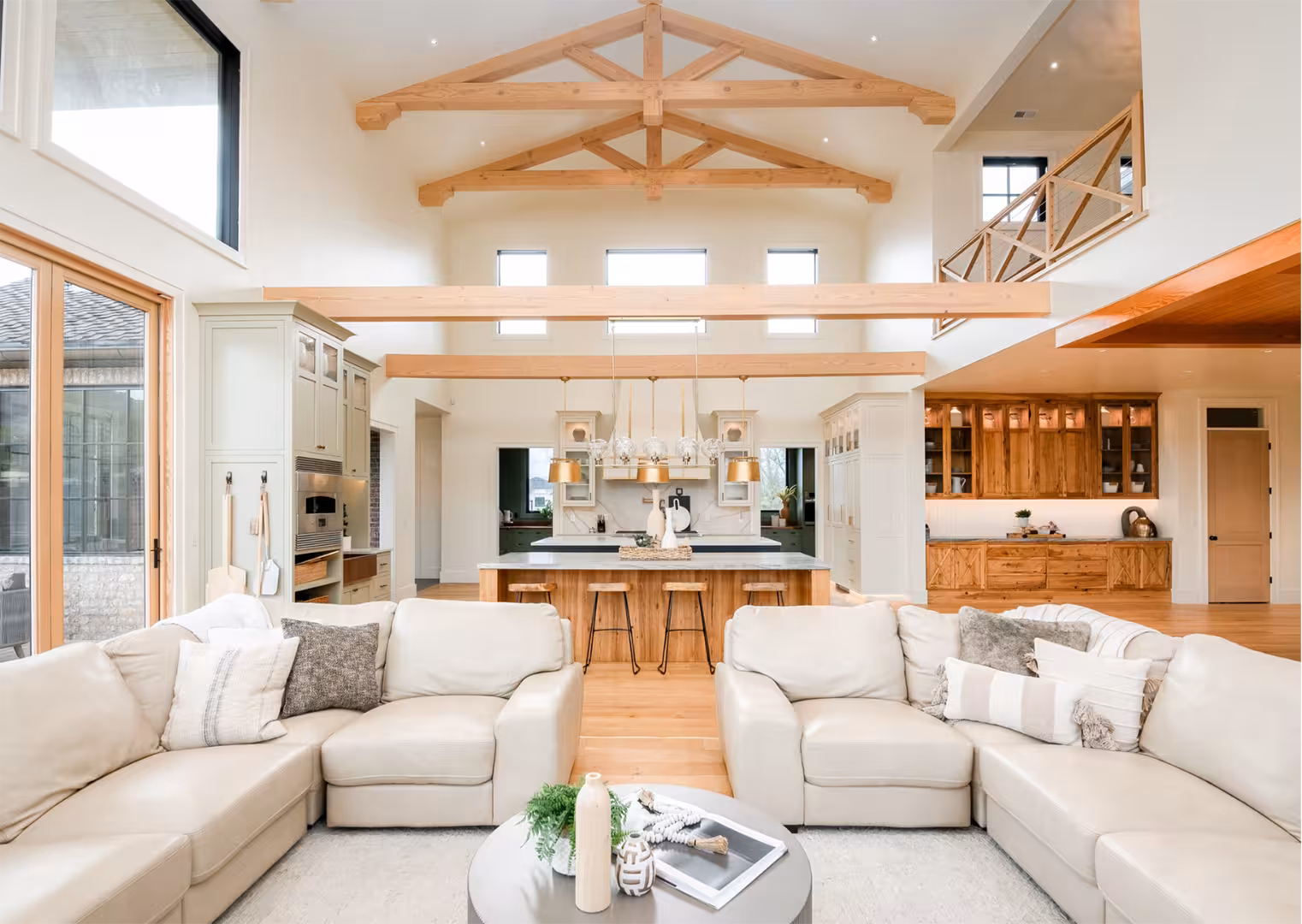 Great room in the Draper home with exposed wood trusses, white sofas and an open kitchen beyond