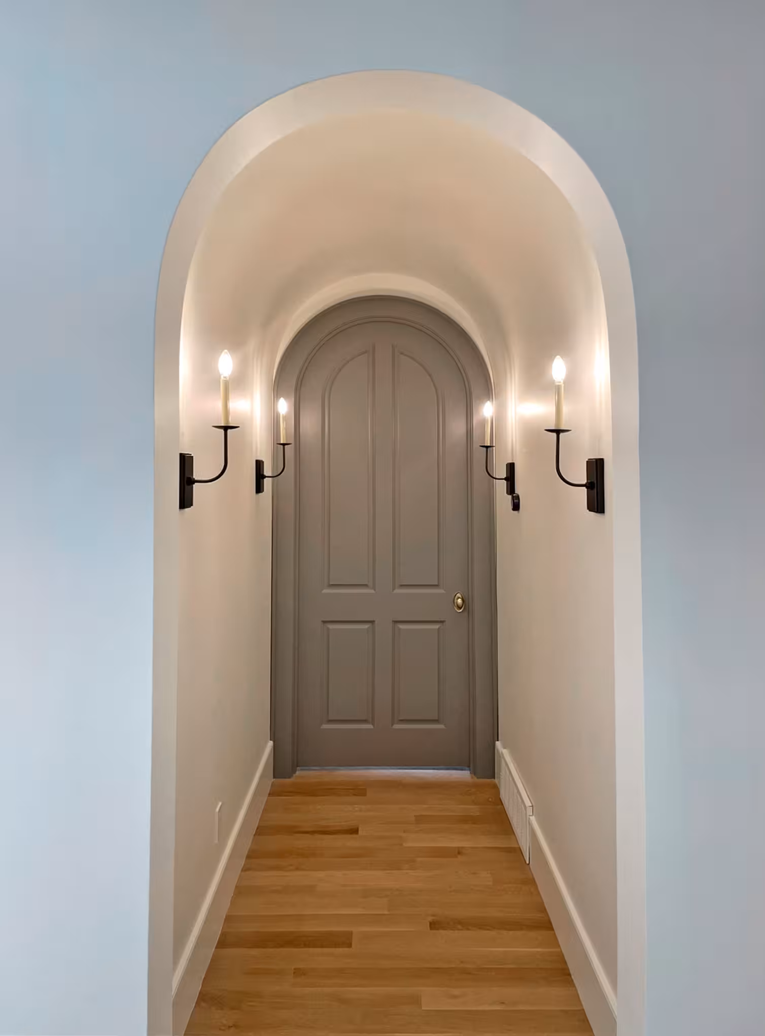Arched hallway in the Holladay home with candle wall sconces and a gray arched door