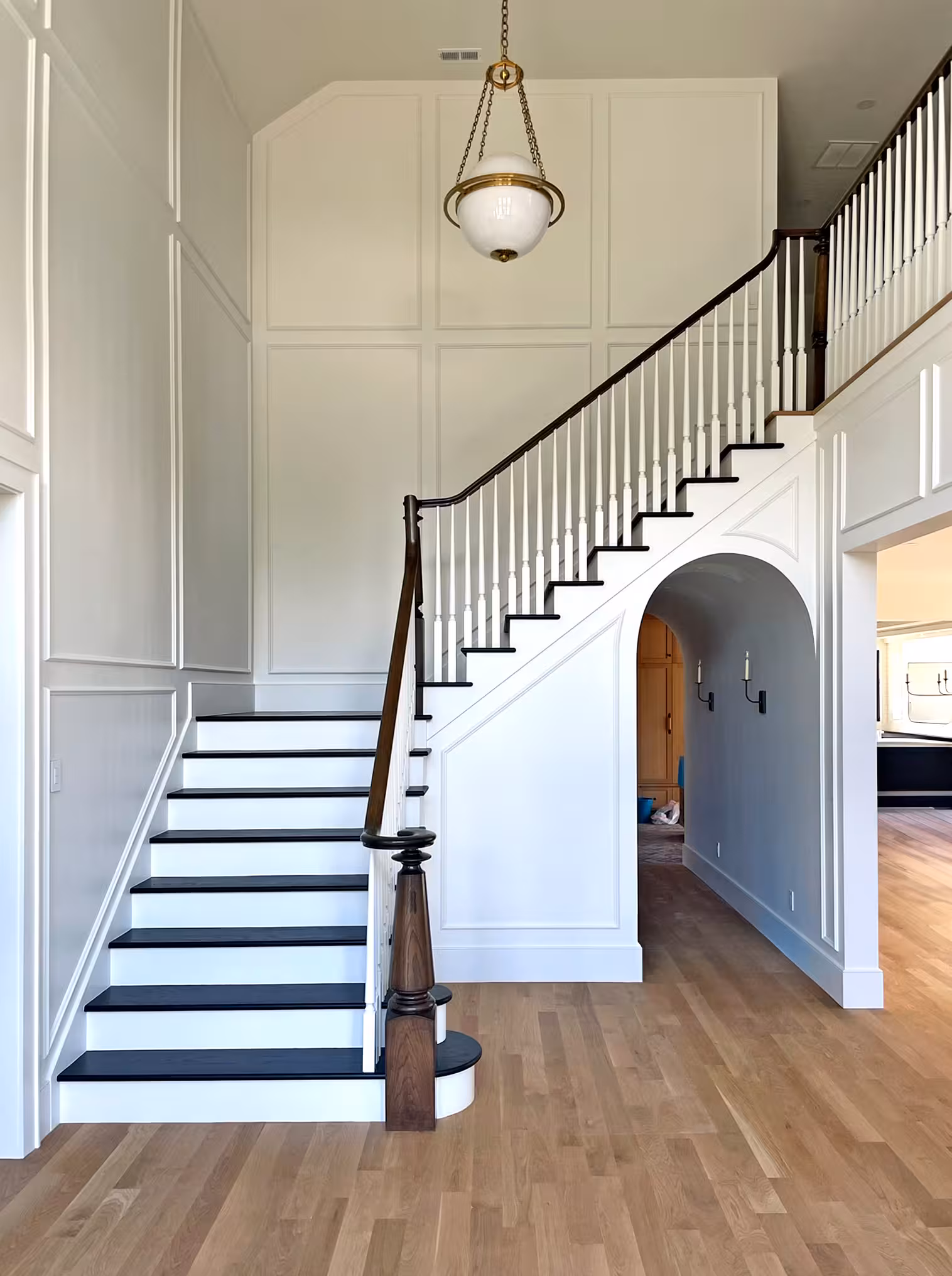 Two-story entry in the Holladay home with a curved white staircase, black treads and paneled walls
