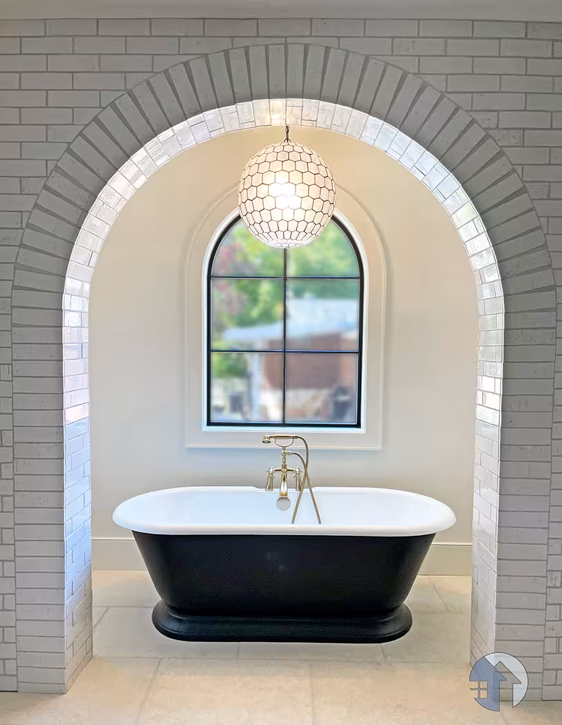 Black freestanding tub under a brick archway and arched window in the Holladay home