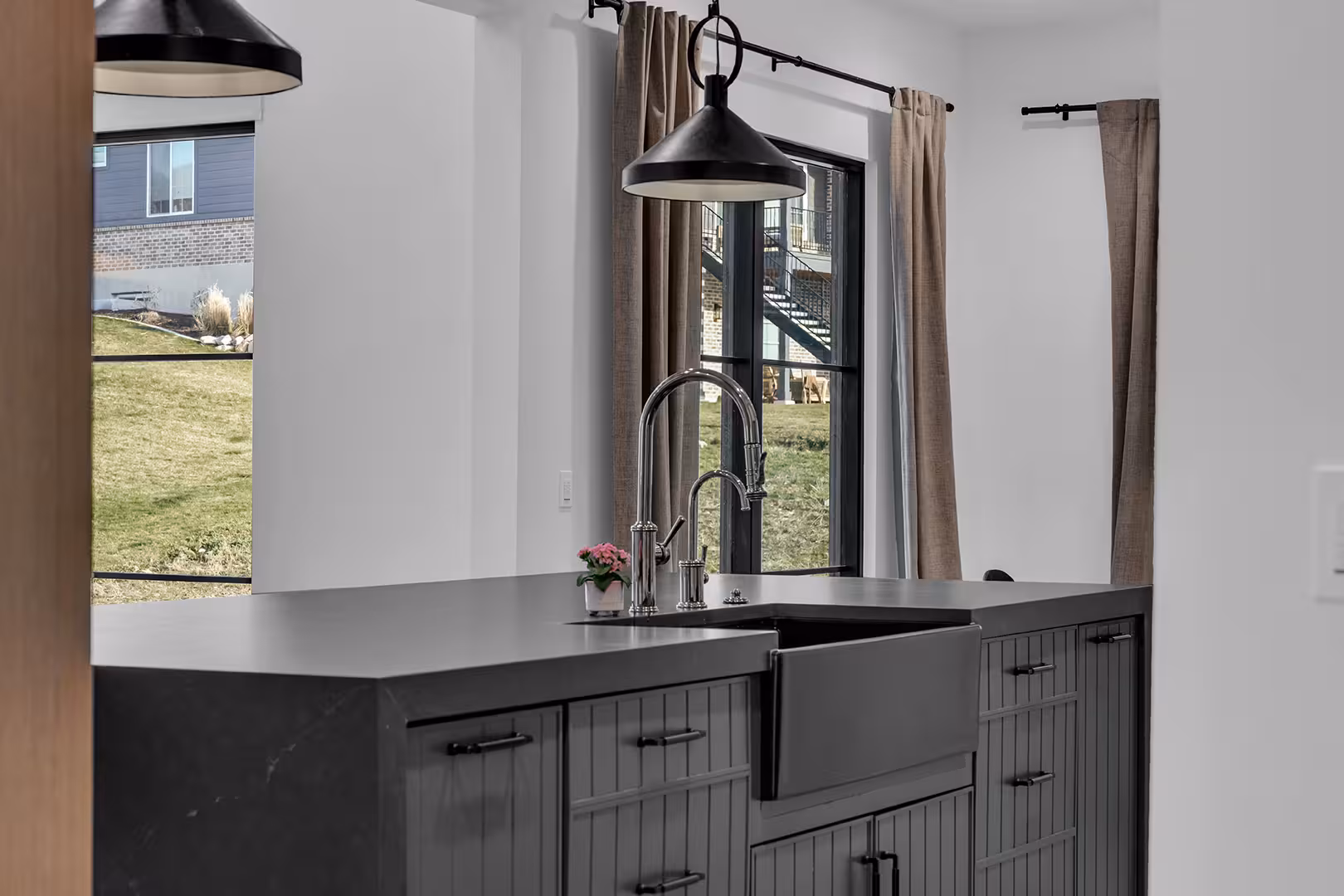 Black farmhouse sink in the dark island of the Elk Ridge kitchen, below a black pendant