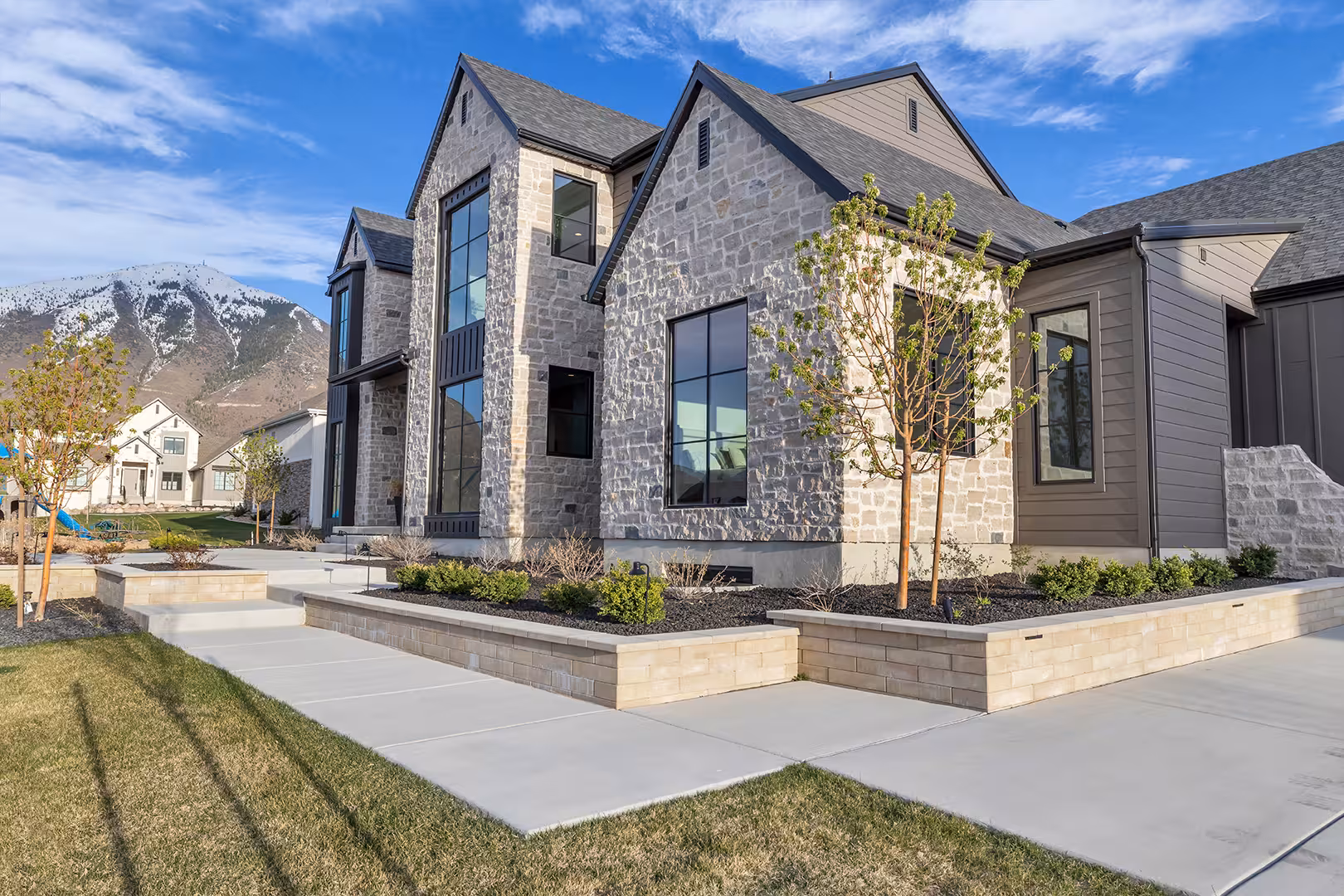 Stone and dark siding facade of the Elk Ridge home with tall black windows and a mountain behind