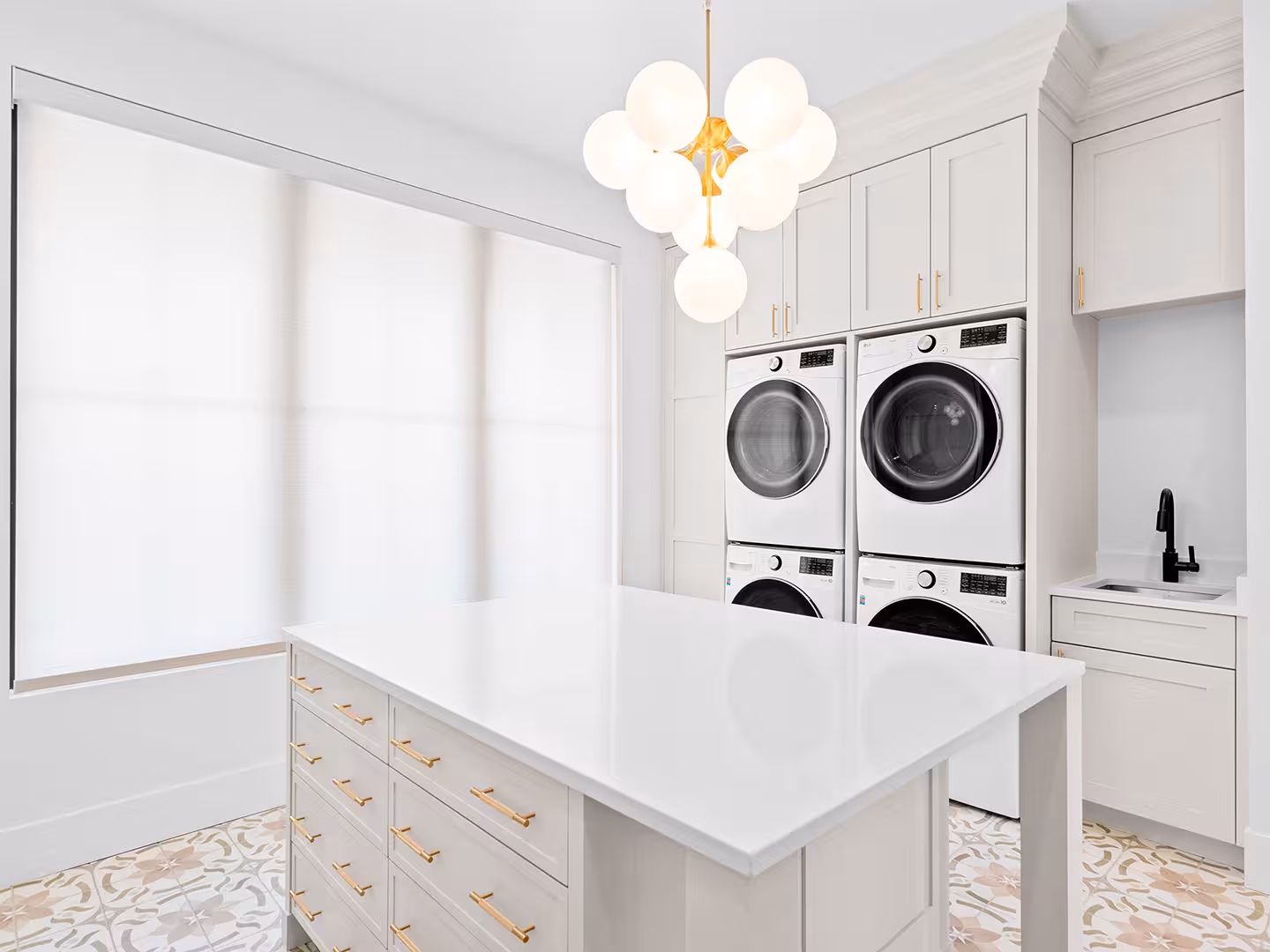 Laundry room in the Lehi home with stacked washers and dryers, a folding island and patterned tile