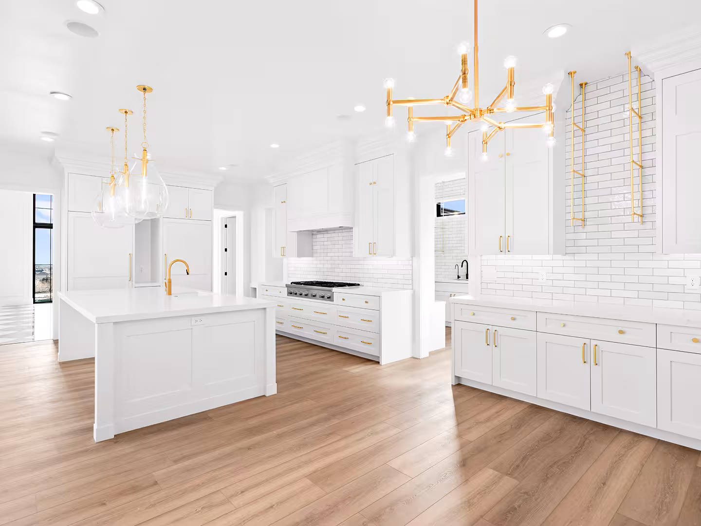 Lehi home kitchen with two white islands, a brass chandelier and brass pot rails