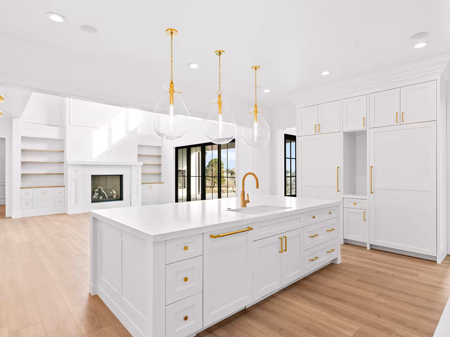 White kitchen island in the Lehi home with brass hardware and clear glass pendants