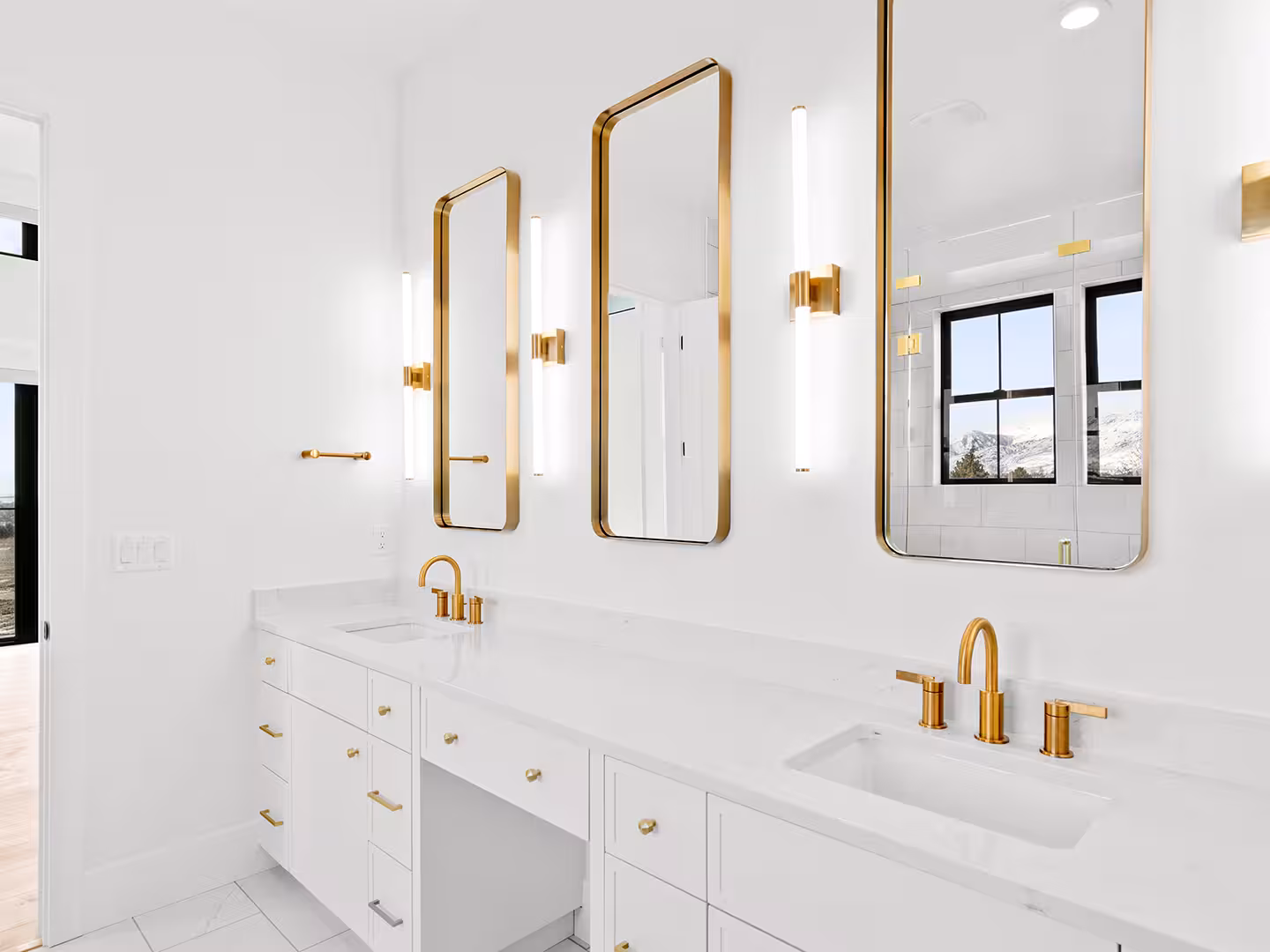 Lehi bathroom vanity with brass-framed mirrors, vertical sconces and gold faucets