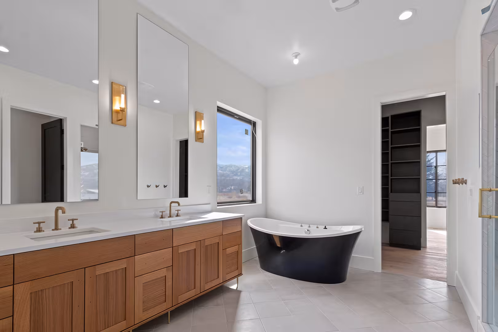 Meadow home bathroom with a wood double vanity, brass faucets and a black freestanding tub