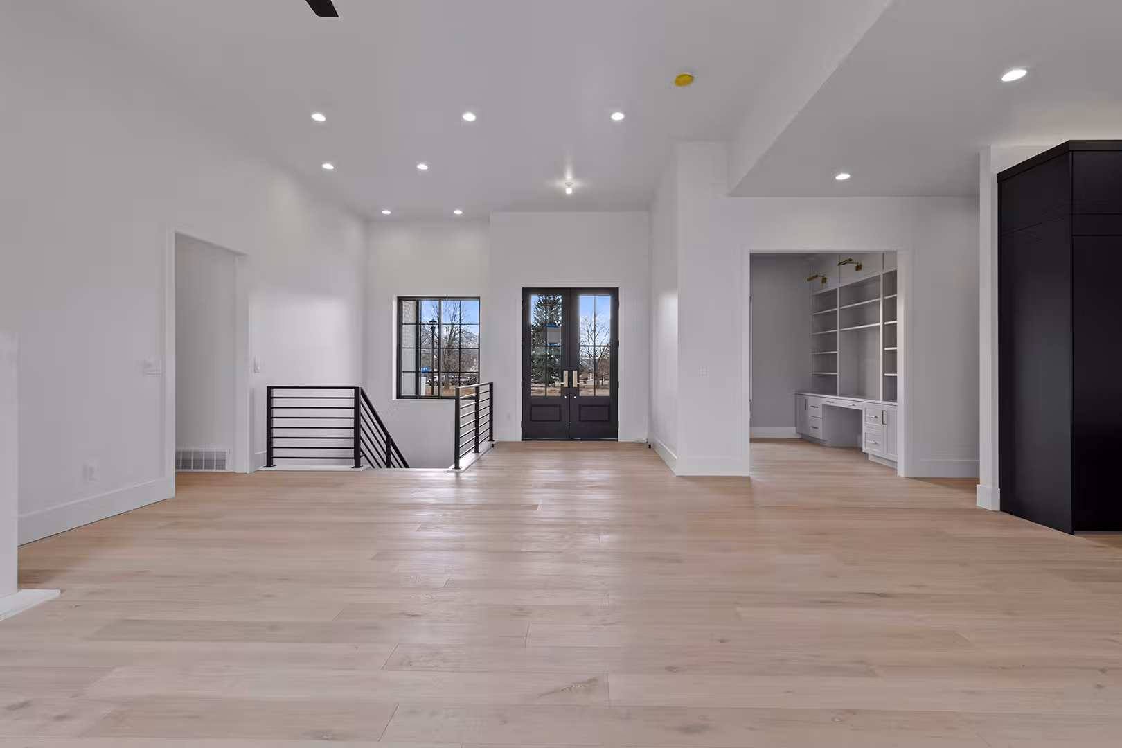 Main floor of the Meadow home with light wood floors, a black stair railing and glass entry doors