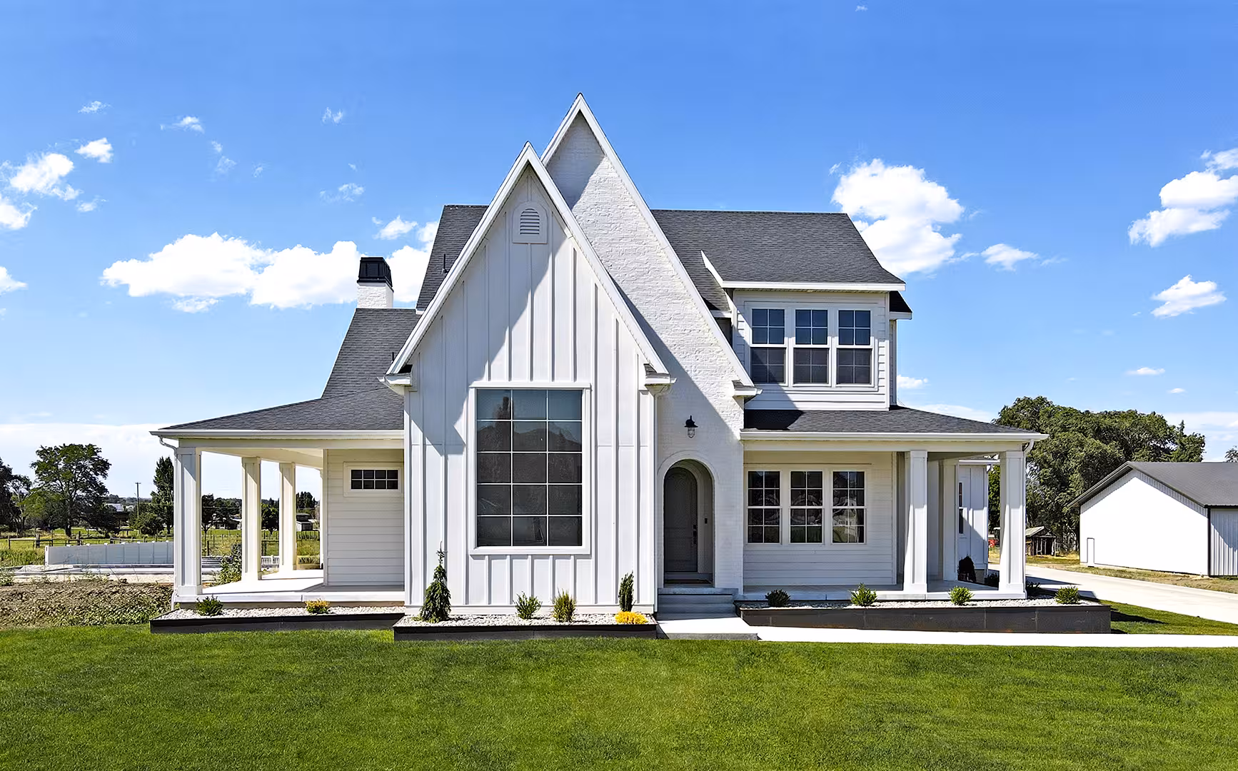 Front of the Paradise home with white board and batten siding, a steep gable and a wraparound porch