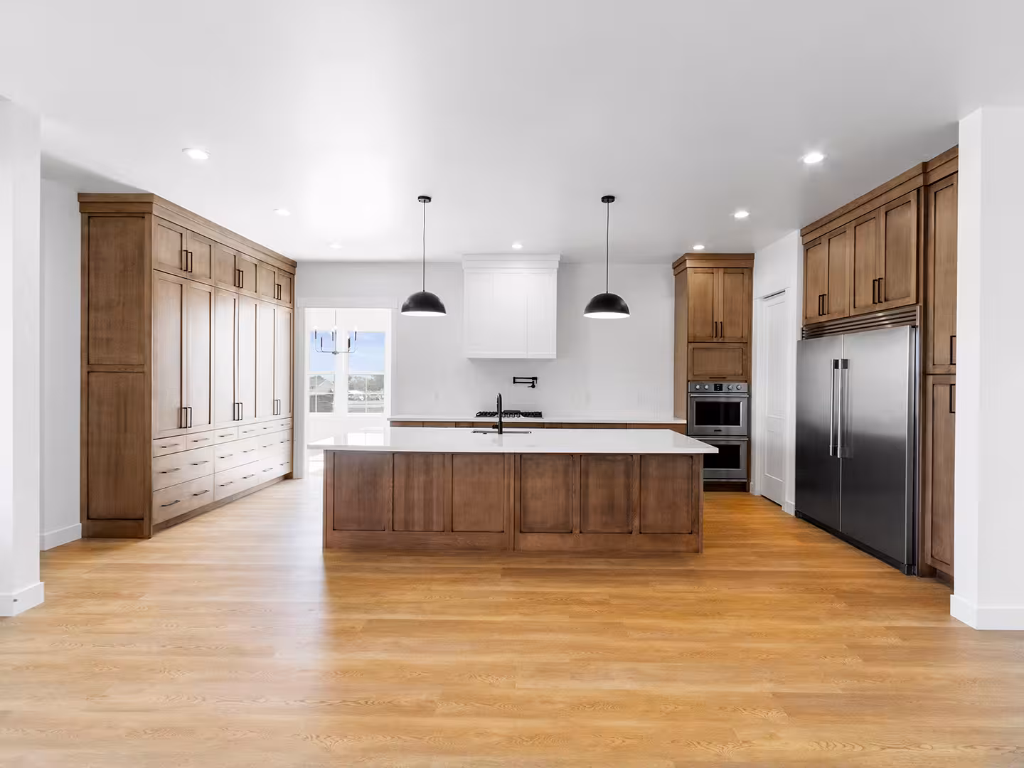 Paradise home kitchen with stained wood cabinets, a large island and black dome pendants