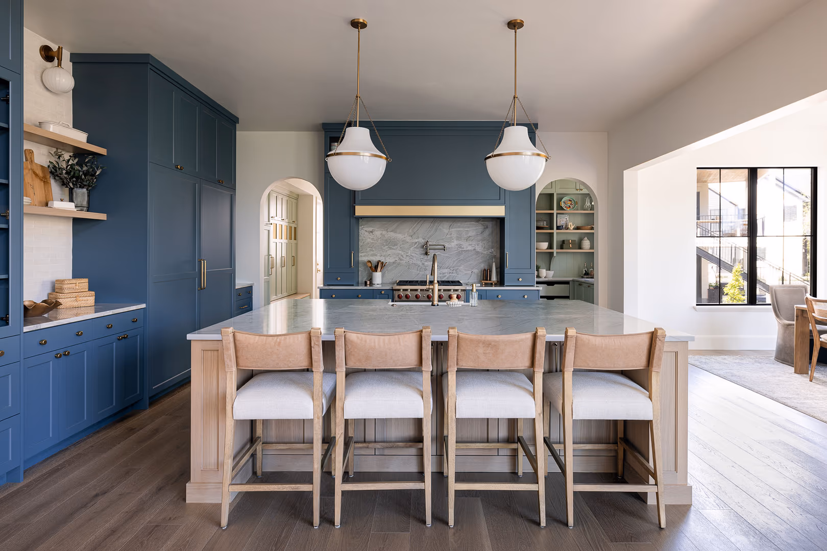 Light wood island with upholstered stools in front of the blue range wall in the Perry kitchen