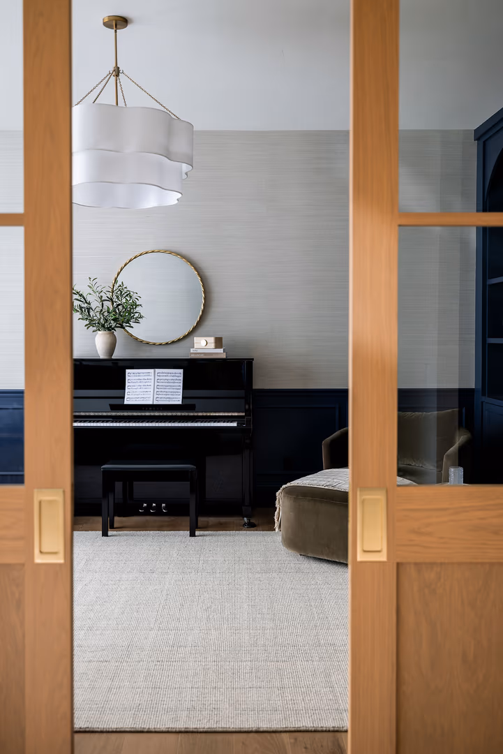 View through wood doors into the Perry piano room with navy wainscot and grasscloth walls