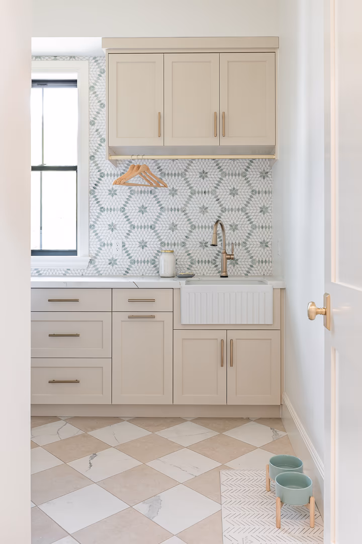 Laundry room in the Perry home with a farmhouse sink, cream cabinets and hexagon tile