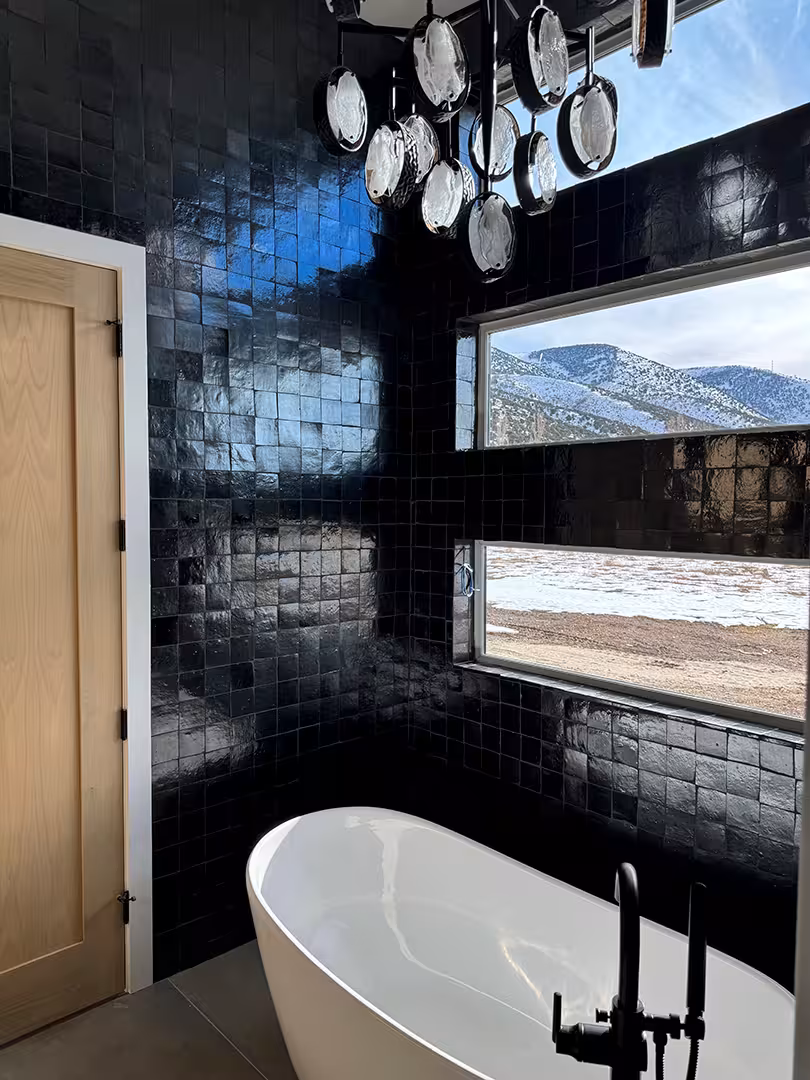 Plymouth bathroom with glossy black tile, a white freestanding tub and a long window