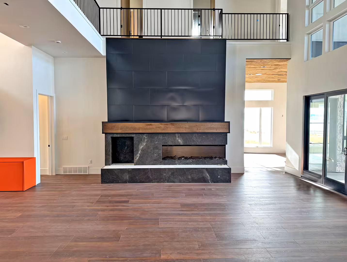 Plymouth great room with a black fireplace wall, a wood mantel and an upstairs railing
