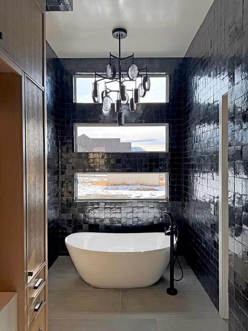 Freestanding tub under stacked windows and a chandelier in the black-tiled Plymouth bathroom