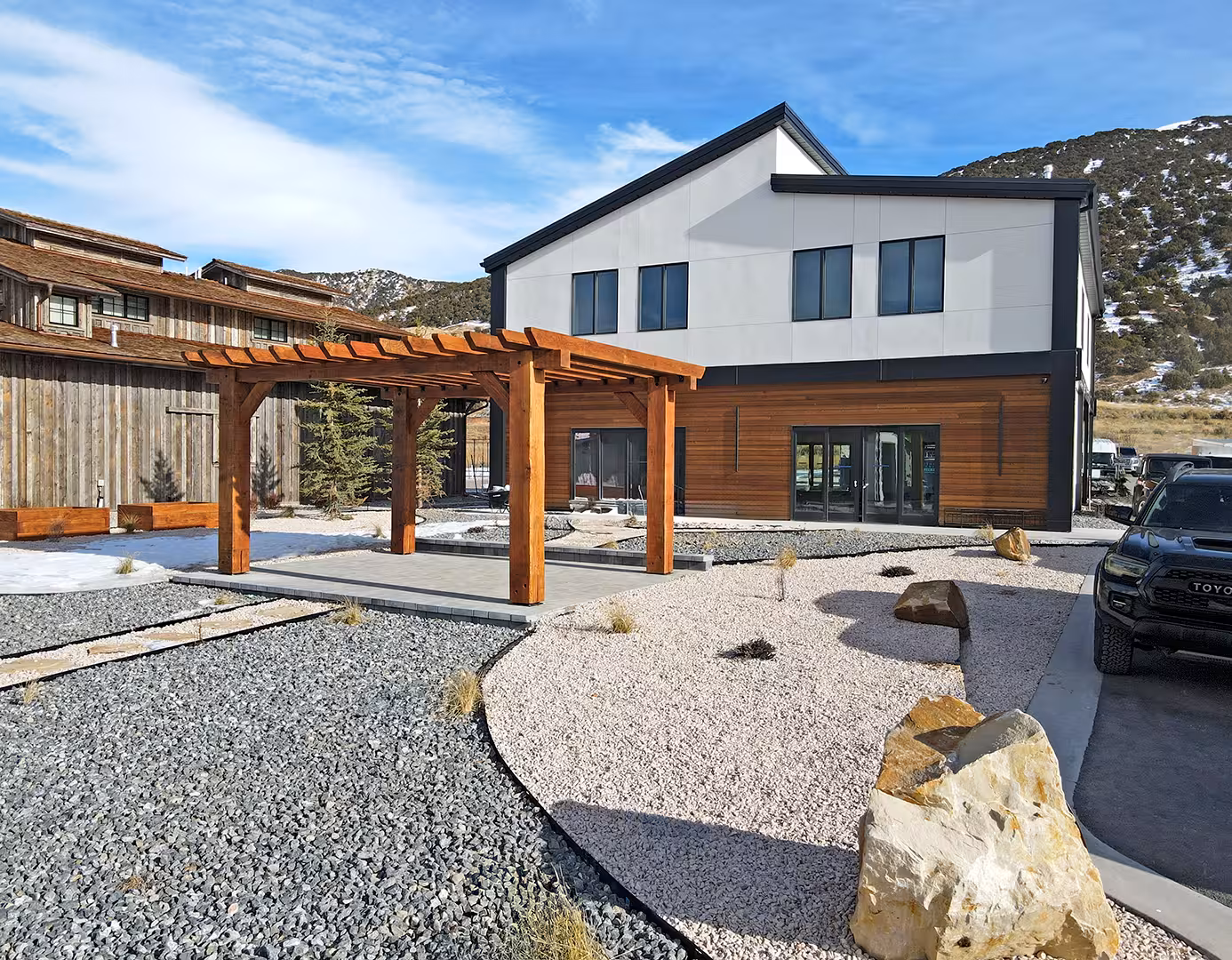 Wood pergola in the gravel courtyard beside the Plymouth home, with hills behind