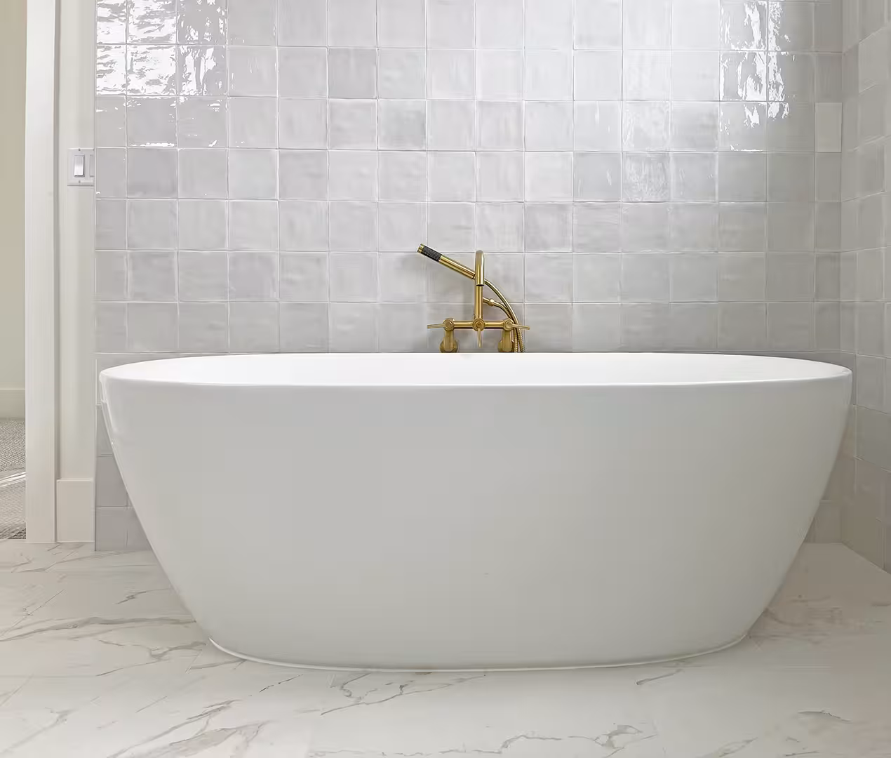 Freestanding tub with a brass filler against white zellige-style tile in the Syracuse home