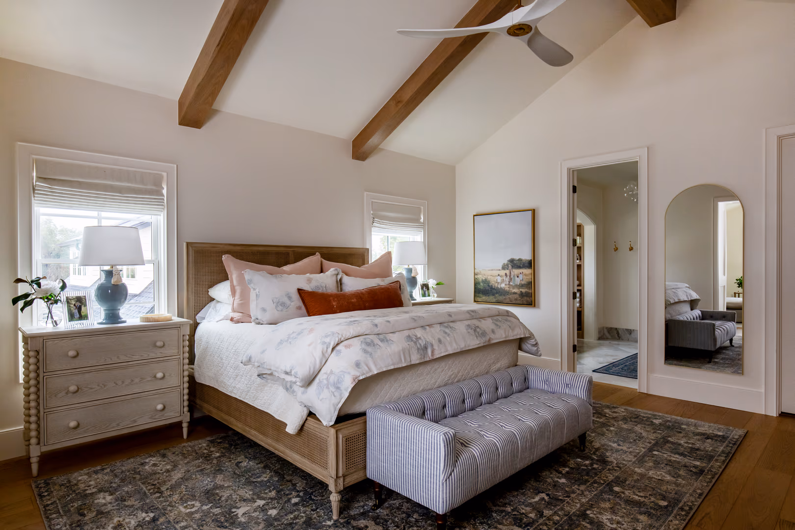 Primary bedroom in the Vineyard home with a vaulted ceiling, wood beams and an arched mirror