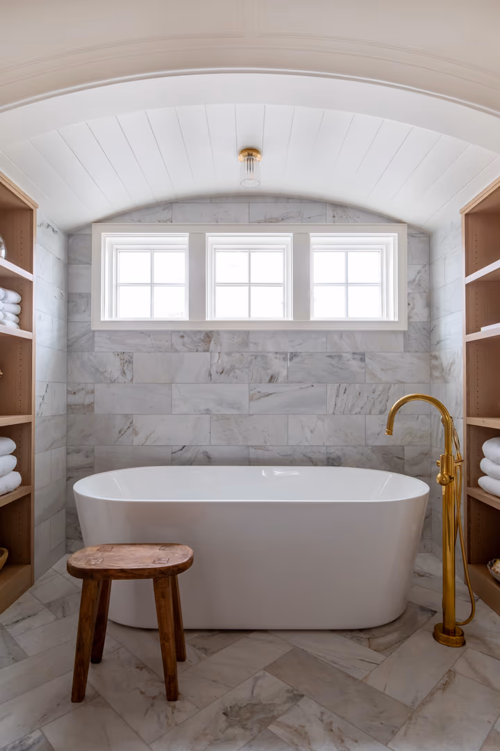 Freestanding tub with a brass floor faucet in a marble-tiled alcove in the Vineyard home