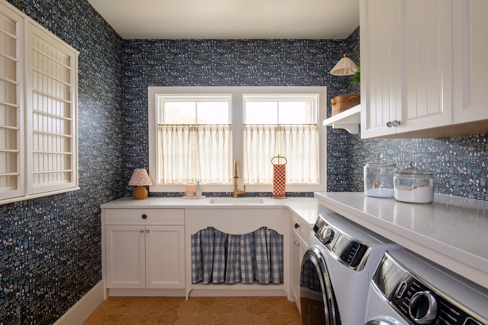 Vineyard laundry room with blue floral wallpaper, a gingham sink skirt and terracotta tile