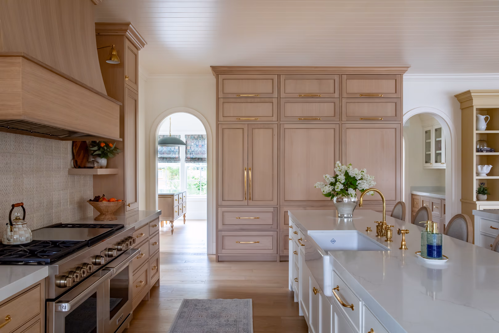 Vineyard home kitchen with a wood range hood, light wood cabinets and arched doorways