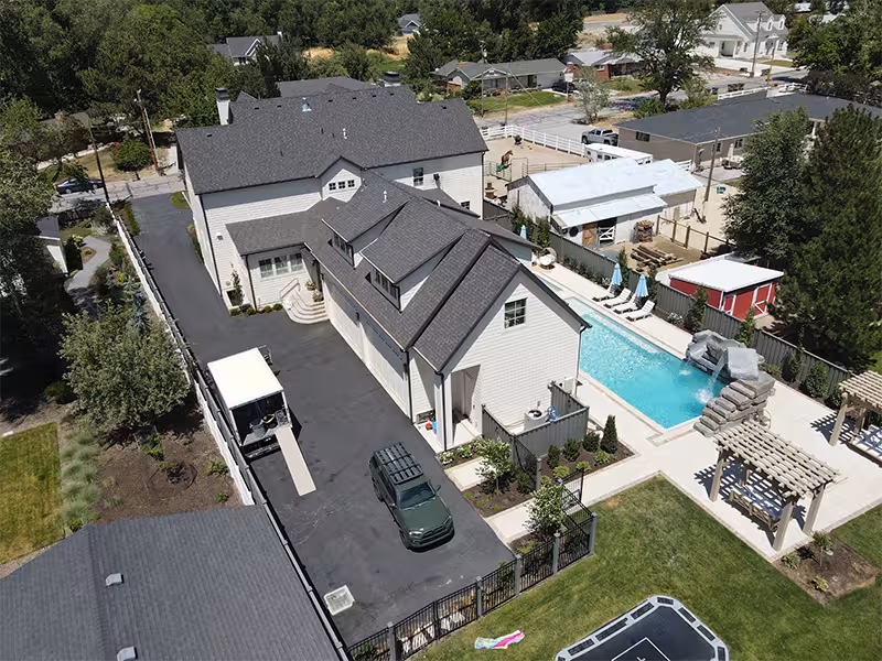 Aerial drone photo of a home with a backyard pool and a long driveway